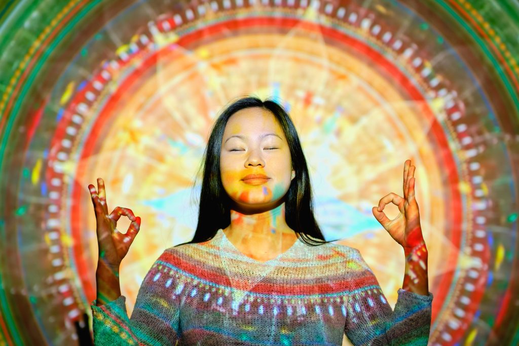 Person meditating with eyes closed, hands in a mudra gesture, surrounded by a colorful, circular light pattern in the background. #SamplePost3.