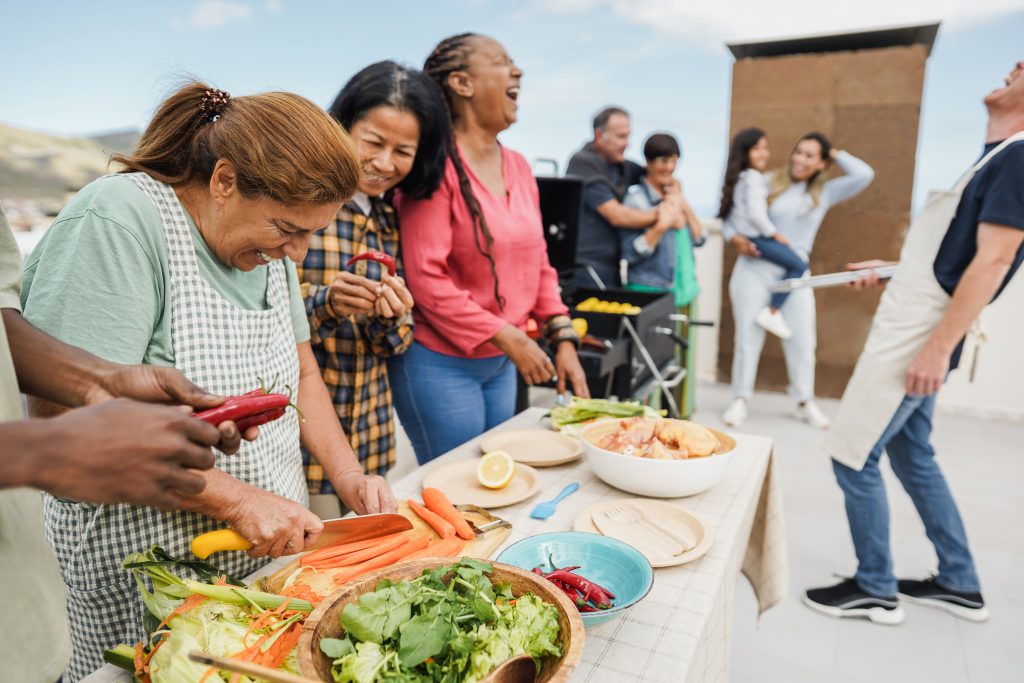 People preparing food and socializing outdoors around a table with vegetables and a grill, capturing the essence of a perfect sample post for summer gatherings.